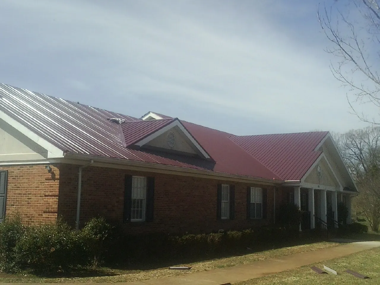 Red metal roof with gabled entries on a long brick building, from a Hail Damage Roof Repair job in Spokane