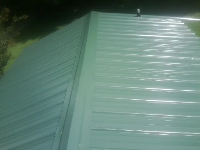 New green metal panels meeting at the ridge of a roof — Flat Roof Repair work by our crew in Spokane