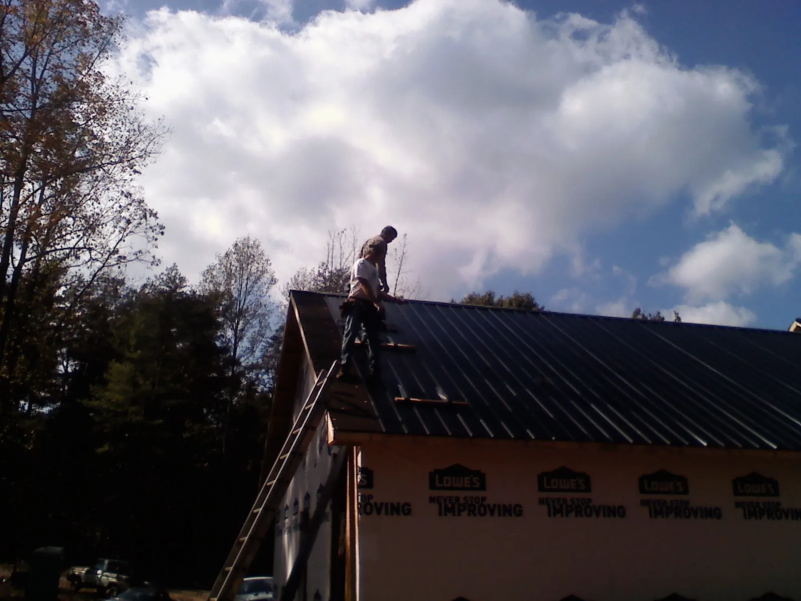 Roofer fastening dark metal panels high against a cloudy sky, from a Roof Inspection job in Spokane