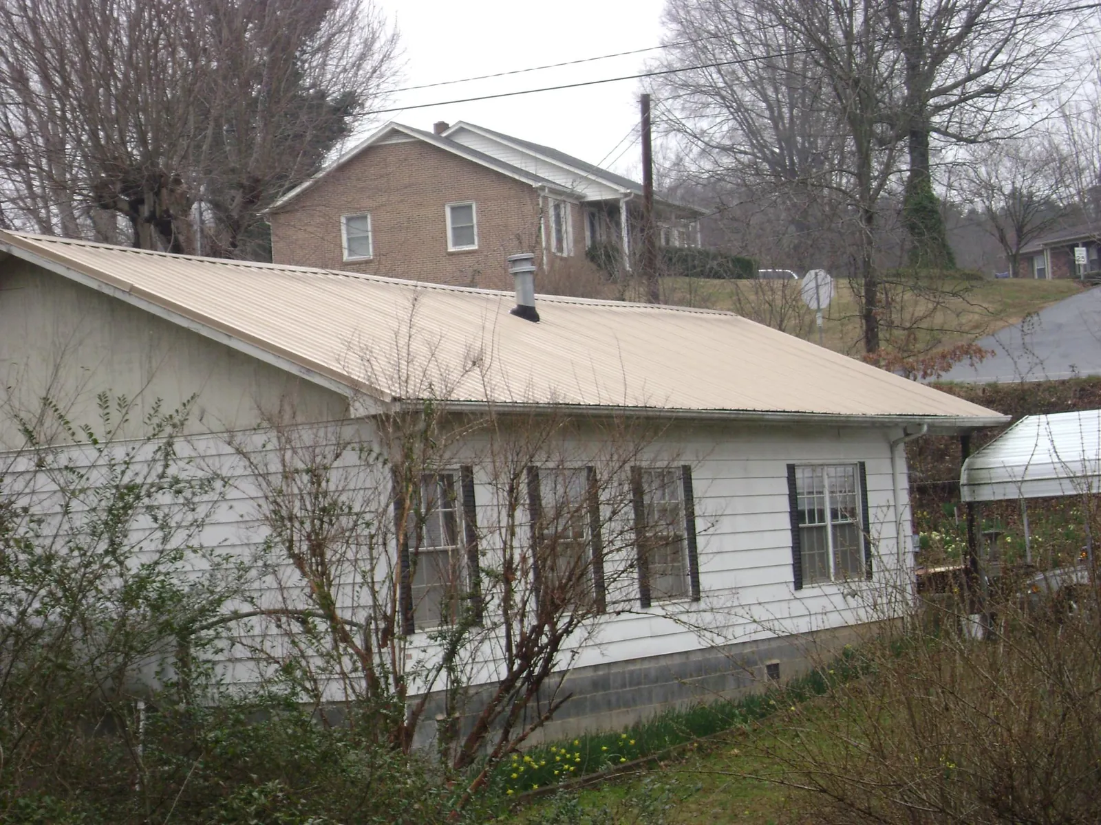 Tan metal roof on a white sided house set into a hillside — Commercial Roofing by Roofing Brothers in Spokane